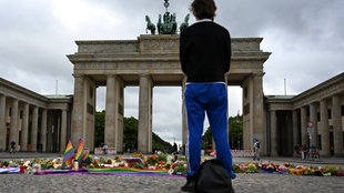 in Mensch steht vor dem Brandenburger Tor, wo nach dem Anschlag auf den CSD Blumen, Kerzen und persönliche Botschaften niedergelegt worden sind.