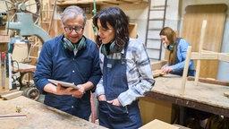Ein älterer Mann und eine jüngere Frau arbeiten gemeinsam in einer Holzwerkstatt