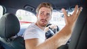 Ein Mann beschwert sich beim Autofahren über andere Verkehrsteilnehmer. 