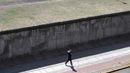 Eine Joggerin läuft vor einem der wenigen noch erhaltenen Abschnitte der Berliner Mauer.