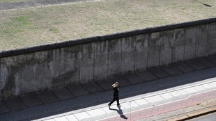 Eine Joggerin läuft vor einem der wenigen noch erhaltenen Abschnitte der Berliner Mauer.