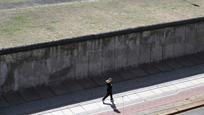 Eine Joggerin läuft vor einem der wenigen noch erhaltenen Abschnitte der Berliner Mauer.