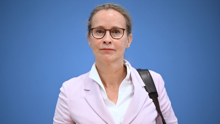 Die Porträtaufnahme zeigt Frauke Brosius-Gersdorf mit Zopf und Brille, den Blick direkt in die Kamera gerichtet – vor blauem Hintergrund.