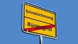 Ein Ortsschild trägt die Aufschrift "Grundsicherung", darunter ist "Bürgergeld" rot durchgestrichen.