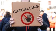 Ein Mensch hält ein Schild mit dem Aufruf zu einem Catcalling-Verbot in die Kamera.