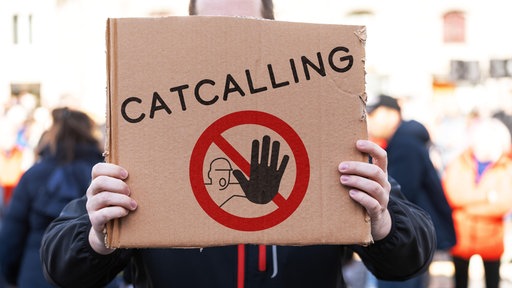 Ein Mensch hält ein Schild mit dem Aufruf zu einem Catcalling-Verbot in die Kamera.