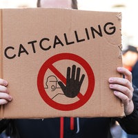 Ein Mensch hält ein Schild mit dem Aufruf zu einem Catcalling-Verbot in die Kamera.