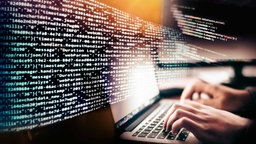 Symbolbild Sicherheit im Netz: Programmcode und Hände mit der Tastatur eines Computers