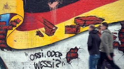 Passanten gehen am 02.10.2015 in Berlin an an einem Wandbild mit der deutschen Nationalflagge und dem Schriftzug "Ossi oder Wessi? vorbei. 