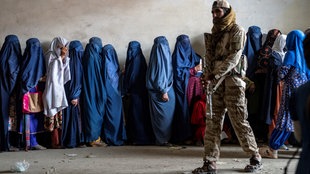 Bewacht von einem Taliban-Soldaten warten verschleierte Frauen in Afghanistan in einer Schlange auf Lebensmittelrationen.