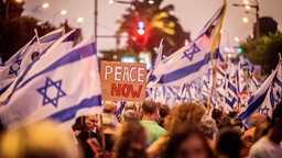 Demonstranten in Tel Aviv halten israelische Flaggen und ein Schild mit der Aufschrift "Peace Now" in die Höhe.