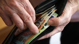 Eine Hand zieht Geldscheine aus einem Portemonnaie.