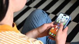 Eine Jugendliche sitzt auf dem Boden und nutzt ein Smartphone - auf dem Display sind verschiedene Apps zu sehen.