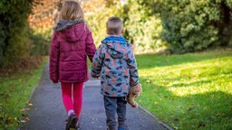 Zwei Kinder gehen in einem Park einen Weg entlang. 