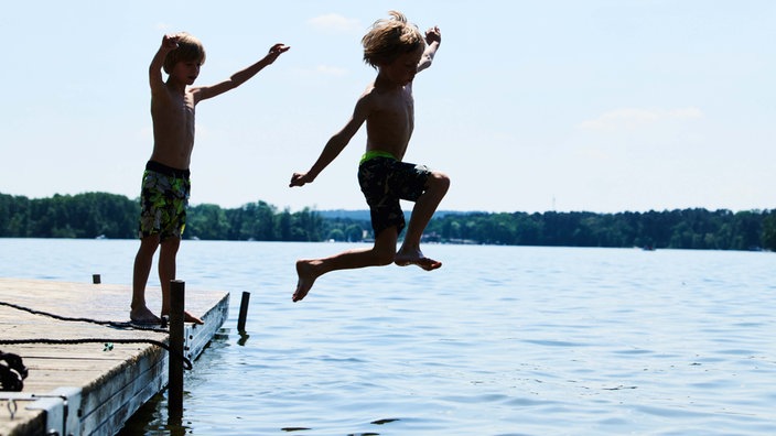 Zwei Kinder spielen am Steg an einem See. 