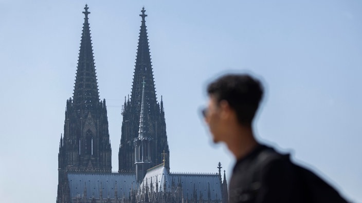 Ein Mann mit Sonnenbrille blickt in Richtung Kölner Dom. 