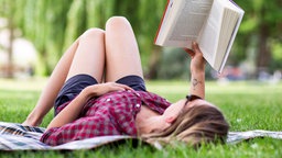 Eine Person liegt entspannt auf einer Wiese und liest ein Buch.