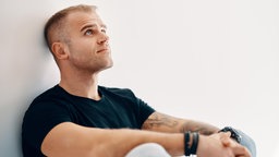 Porträt eines sitzendes Mannes mit kurzen blonden Haaren.