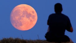 Mann betrachtet rötlich schimmernden Vollmond