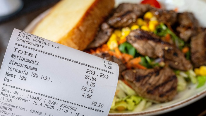 Eine Rechnung mit Mehrwertsteuer neben einem vollen Teller in einem Restaurant.