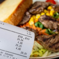 Eine Rechnung mit Mehrwertsteuer neben einem vollen Teller in einem Restaurant.