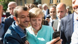 Angela Merkel (CDU) lässt sich am 10.09.2015 für ein Selfie zusammen mit einem Flüchtling fotografieren.