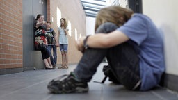 Ein Junge wird von Mitschülerinnen gehänselt; Symbolbild zum Thema Mobbing an Schulen