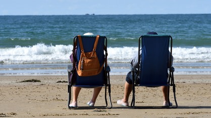 Zwei Rentner genießen in Campingstühlen die Ruhe am Strand – mit weitem Blick aufs Meer.