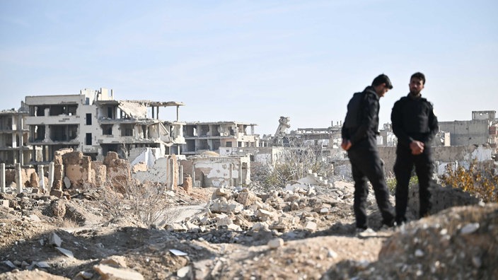 ARCHIV 15.01.2025, Syrien, Damaskus: Sicherheitsmänner stehen im Stadtteil Dschubar während eines Besuchs der Entwicklungsministerin in Syrien vor Ruinen.