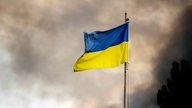 Die ukrainische Flagge ist vor dem Rauch eines Feuers zu sehen, nach Angriffen auf die Ukraine über Kiew.