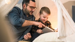 Ein Vater und sein kleiner Sohn lesen zusammen ein Buch.