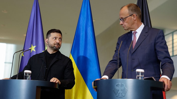 Wolodymyr Selenskyj und Friedrich Merz stehen am 28.05.2025 gemeinsam an Rednerpulten im Bundeskanzleramt und schauen einander stirnrunzelnd an