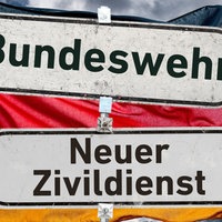 Zwei Wegweiser zeigen in entgegengesetzte Richtungen. Sie tragen die Aufschriften „Bundeswehr“ und „Zivildienst“; im Hintergrund ist eine Deutschlandflagge zu sehen.