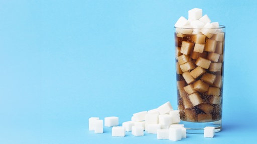 Ín einem Glas befindet sich ein brauner Softdrink und zahlreiche Zuckerwürfel.
