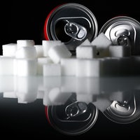 Zwei Getränkedosen mit Softdrinks und zahlreiche Zuckerwürfel liegen auf einem Tisch.
