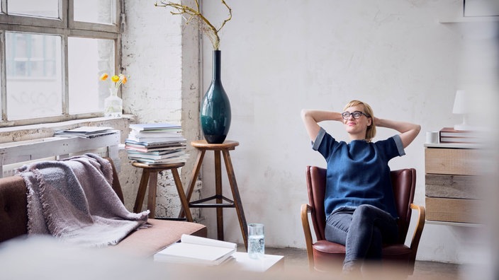 Eine Frau sitzt zurückgelehnt in einem Sessel in einem modern eingerichteten Zimmer.