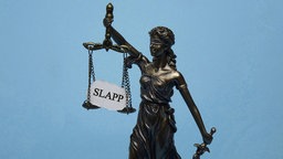 Das Modell der Justitia traegt den Schriftzug "SLAPP".
