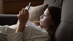 Ein trauriges Mädchen liegt mit einem Smartphone in der Dunkelheit.