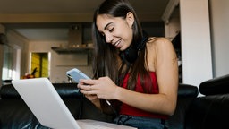 Mädchen mit Laptop und Mobiltelefon sitzend auf dem Sofa.