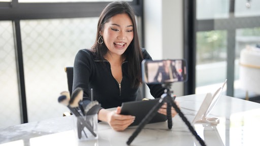 Attraktive asiatische Beauty-Influencerin schminkt sich und filmt ein Make-up-Tutorial mit ihrem Smartphone.