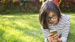 Ein Mädchen  liegt auf einem Rasen und nutzt ein Smartphone 