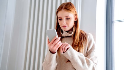 Lächelndes Teenager-Mädchen benutzt zu Hause ein Smartphone. 