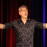 Christoph Sieber auf der Bühne vom Kulturforum Heinrich Heine Schulzentrum Ostheim mit ausgebreiteten Armen