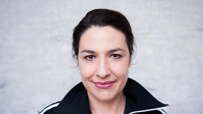 Portrait der Kabarettistin Eva Eiselt vor hellem Hintergrund, sie lächelt in die Kamera