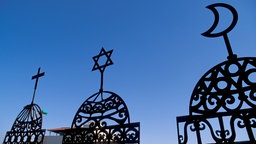 Kreuz, Stern, Halbmond jeweils auf stilisierten Kuppeln