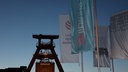 Die Zeche Zollverein ist am Abend beleuchtet zu sehen und Fahnen des Literaturfestivals lit.RUHR