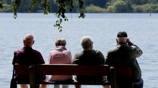 Urlauber sitzen bei sommerlichem Wetter auf Bank