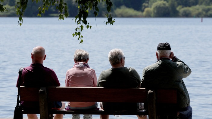 Urlauber sitzen bei sommerlichem Wetter auf Bank