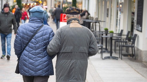 Ein älteres Paar geht Arm in Arm durch eine Einkaufsstraße