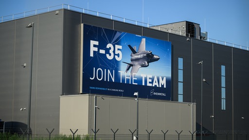 Produktionshalle von Rheinmetall von außen mit einem Banner "F-35. JOIN THE TEAM"